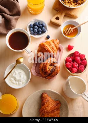 Ein herrliches Frühstücksangebot mit frischen Croissants, lebendigen Himbeeren und Blaubeeren, cremigem Joghurt, Honig, knuspriger Granola, Kaffee und Erfrischung Stockfoto