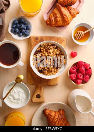 Ein herrliches Frühstücksbuffet mit einer Schüssel Granola, frischen Croissants, verschiedenen Beeren, Honig und Kaffee, perfekt für ein leckeres Frühstück ex Stockfoto