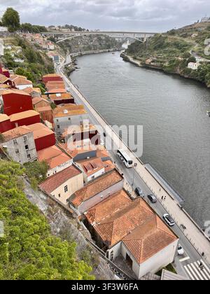 Erhöhte Ansicht von Porto, Portugal entlang des Douro-Flusses, mit terracottafarbenen Dächern, Uferstraße und Verkehr sowie einer Betonbogenbrücke unter bewölktem Himmel Stockfoto