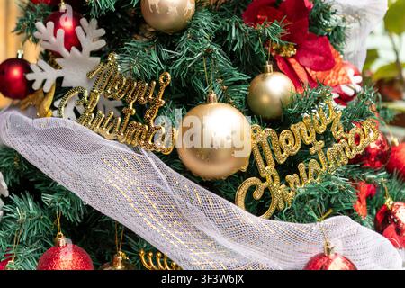Nahaufnahme eines geschmückten Weihnachtsbaums mit goldenen und roten Kugeln, glitzernd, Frohe Weihnachten, Verzierung, Band und Poinsettia-Akzente, die eine festliche Atmosphäre schaffen Stockfoto