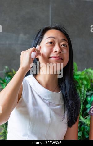 Nahaufnahme-Porträt einer jungen Frau, die sanft einen Jade-Gesichtsweller auf ihrer Wange verwendet und natürliche Hautpflege und Selbstfürsorge in einer ruhigen Innenumgebung praktiziert Stockfoto