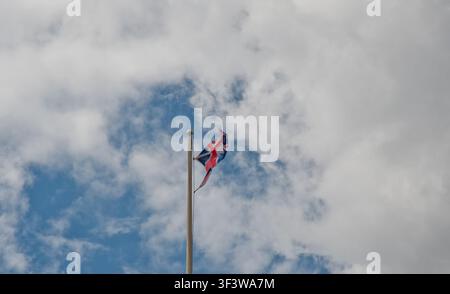 Union-Jack-Flagge, die an einer Flaggenstange vor einem dramatischen bewölkten Himmel mit blauem Hintergrund weht Stockfoto