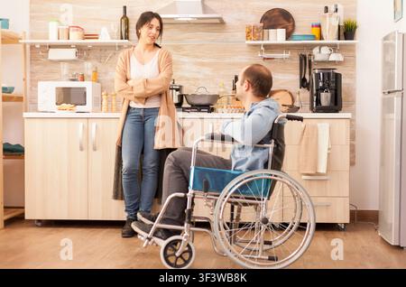 Behinderter Mann im Rollstuhl verbringt Zeit mit Frau in der Küche. Behinderter gelähmter behinderter Mann mit Gehbehinderung, der sich nach einem Unfall integriert. Stockfoto