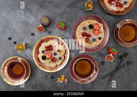 Kreative Overhead-Frühstücksszene mit Pfannkuchen, Obst und Teetassen in ausgewogener Komposition Stockfoto