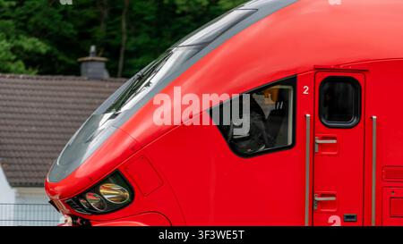 Nahaufnahme eines modernen roten Personenzugs in Deutschland, der die Führerstandsfront und die Seitentür des Regionalverkehrs zeigt. Stockfoto