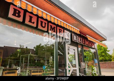 Kleine örtliche Blumenladen-Fassade mit einem gestreiften orangefarbenen Vordach und Schriftzug in einer europäischen Stadt unter einem bewölkten Himmel. Stockfoto
