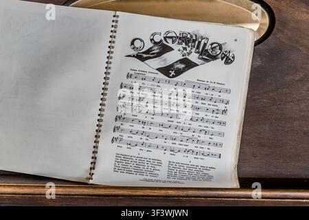 Ein offenes Songbuch mit dem Lied „Ô Carillon“ liegt in einem historischen Gebäude im Akadischen Historischen Dorf von Nova Scotia an der Old Church Road in Lower West Pubnico, Nova Scotia. Der Text wurde vom Quebec-Dichter Octave Crémazie geschrieben, und die Melodie wurde von Ch. W. Sabattier komponiert – das Lied feiert die historische Carillon-Flagge als frühes Symbol der frankokanadischen Identität. Argyle Municipal, Nova Scotia, Kanada Stockfoto