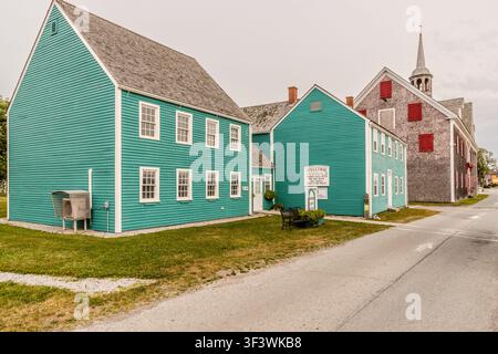 Türkisfarbene historische Gebäude, die ein Museum und ein Geschenkeladen beherbergen, säumen Charlotte Lane im historischen Hafenviertel von Shelburne, Nova Scotia; im Hintergrund ist der Turm einer Kirche zu sehen. Shelburne, Nova Scotia, Kanada Stockfoto
