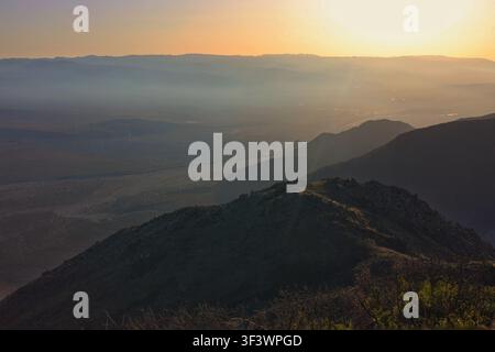 Goldener Sonnenuntergangsglanz über einem dunstigen Wüstentbecken und silhouettierten Bergkämmen Stockfoto