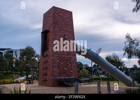 Melbourne, VIC, Australien. 20. Juli 2026. - Ein einzigartiger Kletterturm aus Ziegelsteinen mit einer langen Röhrenrutsche, der in einem modernen Spielplatz während einer ruhigen Dämmerung steht Stockfoto