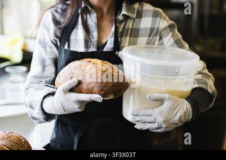 Lächelnde Bäckerin hält frisches handwerkliches Sauerteigbrot in der Bäckerei Stockfoto