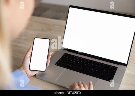 Geschäftsfrau hält Smartphone und verwendet einen Laptop mit weißem leeren Platzhalterbildschirm Stockfoto