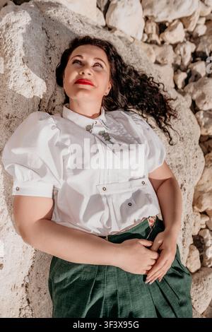 Frau liegt in weißer Bluse und grünem Rock auf sonnigem Kalkstein während eines friedlichen Sommernachmittags Stockfoto