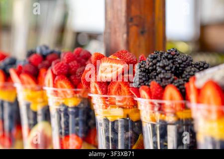 Verschiedene frisch geschnittene Fruchtstücke in klaren Plastikbechern, die auf Ladenregalen angeordnet sind. Gesunde Obstsalatbecher sind zum Verkauf bereit. Lebensmittel Stockfoto