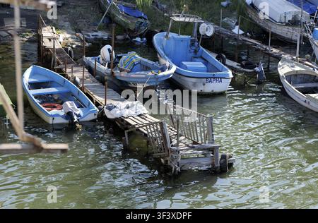 Mehrere Arbeitsefischerboote, die im Wasser liegen, an rustikalen Holzstegen mit alten Seilen und nautischer Ausrüstung befestigt, spiegeln das bescheidene Leben o Stockfoto