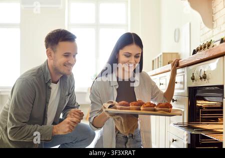 Porträt eines glücklichen Paares, das zusammen in der Küche zu Hause gebackene Muffins aus dem Ofen zieht Stockfoto