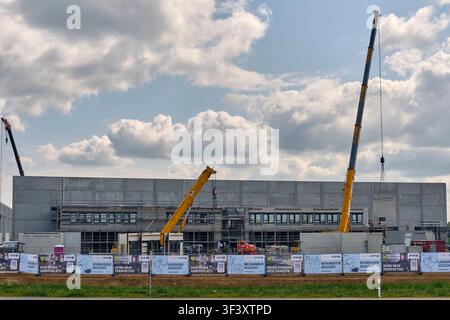 Großes Industriegebäude im Bau mit mehreren Kränen und Gerüsten, die bei bewölktem Himmel in Handewitt, Deutschland, sichtbar sind. Stockfoto