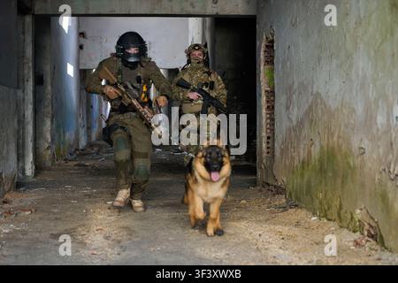 Taktische Soldaten mit Militärhund rennen durch ein verlassenes Gebäude während einer städtischen Trainingsübung Stockfoto