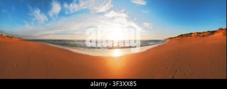 Panoramablick auf einen leeren goldenen Strand und das sanfte Meer unter einem hellen Morgensonneaufgang Stockfoto