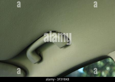 Eine Nahaufnahme des Innenraums eines Autos zeigt den Griff an der Decke und die Stoffverkleidung. Sonnenlicht reflektiert sanft auf den Oberflächen. Stockfoto