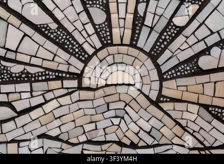 Nahaufnahme von keramischer Mosaikfliesen-Kunst mit strahlendem Sonnenstrahlenmuster, zerbrochenen Fliesenstücken, beiger und grauer Textur Stockfoto