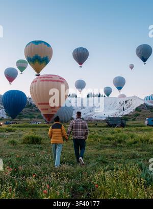 Paar schlendert Hand in Hand durch üppige Felder, während farbenfrohe Heißluftballone den Himmel über Pamukkale, Türkei, füllen. Dieser malerische Ort ist berühmt Stockfoto