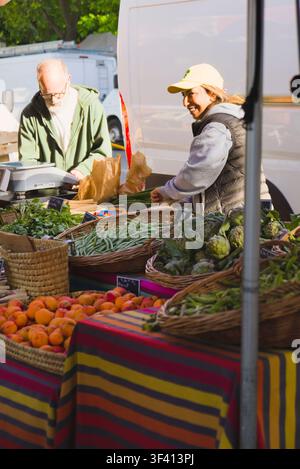 Ein lächelnder Verkäufer, der mit einem Kunden an einem Stand mit frischen Produkten auf einem Markt in Arles, Frankreich, interagiert. Stockfoto