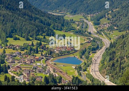 Luftaufnahme des Dorfes Rodi-Fiesso im Tal Leventina, Tessin, Schweiz, mit der Autobahn, der Eisenbahn, einem kleinen See und den umliegenden Bergen Stockfoto