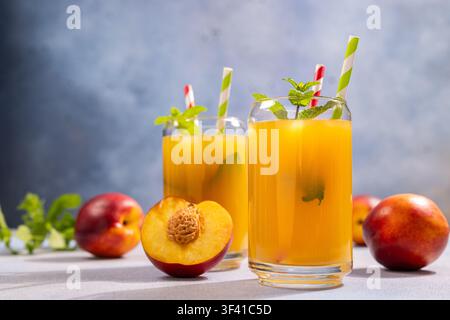 Zwei Gläser süßen Pfirsich- und Nektarinen-Safts mit Eis. Frische Minzblätter. Und gestreifte Strohhalme. Bereit für eine erfrischende Sommererfrischung Stockfoto