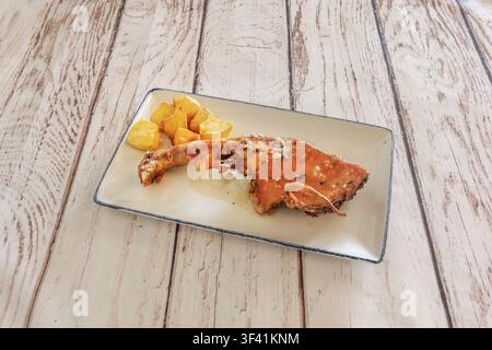 Gebratenes Ferkelbein mit Kräutergarnitur, serviert mit Bratkartoffeln auf einem rechteckigen Teller Stockfoto