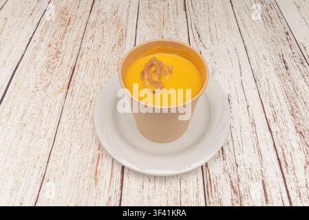 "Cremige Karottensuppe garniert mit karamellisierten Zwiebeln, serviert in einer Kraftpapiertasse" Stockfoto