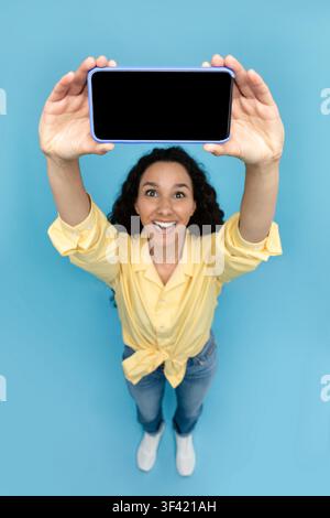 Glückliche junge hispanische Frau hält ein Smartphone mit leerem Bildschirm, Studio. Technologiekonzept Stockfoto