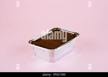 Tiramisu-Dessert mit Kakaopulver in Aluminiumschale auf rosa Hintergrund Stockfoto
