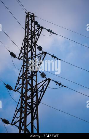 Gitterstahlübertragungsturm, der Hochspannungsleitungen gegen einen blauen Himmel stützt Stockfoto