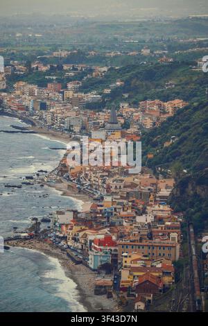Panoramarischer Hochwinkelblick auf die sizilianische Küste mit farbenfrohen Resortgebäuden entlang der Meeresküste in Taormina. Stockfoto