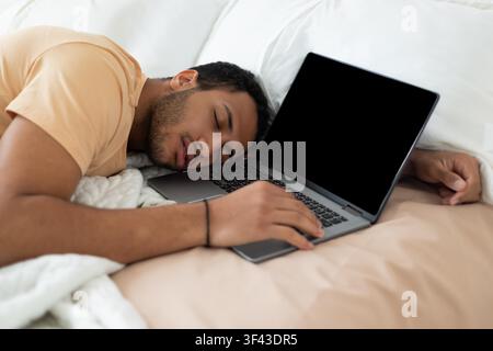 Unerkennbarer Mann schläft mit Laptop auf dem Bett, müde nach langen Arbeitsstunden Stockfoto