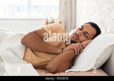 Junger schwarzer Mann schläft friedlich im Bett, entspannt und erholend, Schlafzimmerumgebung Stockfoto