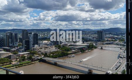 Eine Hochwinkelperspektive fängt eine weitläufige Stadtlandschaft mit einem gewundenen Fluss, schlanken Wolkenkratzern und geschäftigen Brücken unter dramatischen bewölkten Himmeln ein. Stockfoto