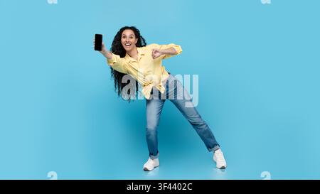 Glückliche junge Frau lächelt und macht Selfie mit Smartphone, blauer Hintergrund, Lifestyle-Konzept Stockfoto