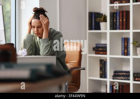 Gestresste junge Frau mit Händen am Kopf am Schreibtisch, die sich in einer Heimarbeitsumgebung überfordert und frustriert fühlt Stockfoto