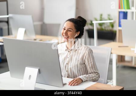 Lächelnde junge hispanische Frau arbeitet am Computer in einem modernen Büro, Geschäftskonzept Stockfoto