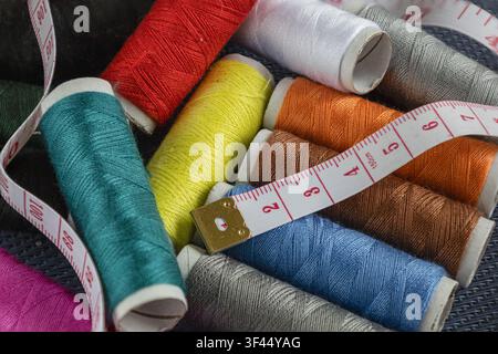 Nahaufnahme von farbenfrohen Nähgarnspulen mit einem flexiblen Maßband, die Schneiderei, Nähen, Modedesign, Handwerk und Textilproduktion darstellen Stockfoto