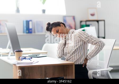 Gestresste junge schwarze Frau, die im Büro am Schreibtisch Nackenschmerzen erlebt, Gesundheitskonzept Stockfoto