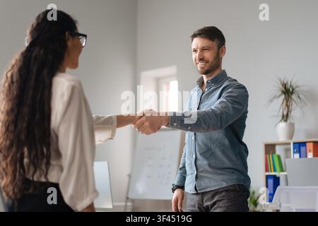 Geschäftsmann, der in einem modernen Büro mit einer Geschäftsfrau Hände schüttelt, professionelle Interaktion Stockfoto