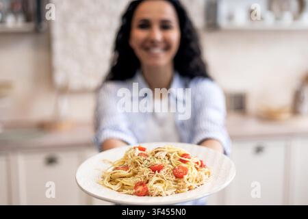 Lächelnde Frau hält einen Teller Pasta mit Kirschtomaten in der Küche, Konzept für gesunde Ernährung Stockfoto