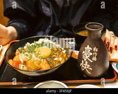 Kaisendon-Reisschale mit rohem Thunfisch, Lachs und Eigelb, serviert mit Misosuppe und einem Sake-Fläschchen in einem Restaurant in Shinjuku, Tokio, Japan Stockfoto