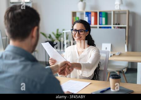 Zufriedene Frau, die während eines Geschäftstreffens im Büro ein Dokument übergibt, Geschäftskonzept Stockfoto