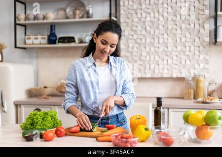 Glückliche junge Frau schneidet frisches Gemüse in einer hellen modernen Küche, Kochkonzept Stockfoto