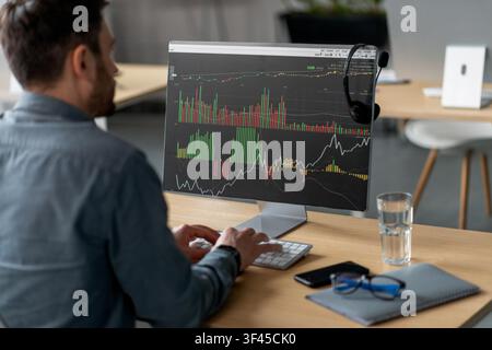 Konzentrierter männlicher Händler analysiert Aktienmarktdaten auf dem Computerbildschirm in einem modernen Büro, nicht zu erkennen Stockfoto