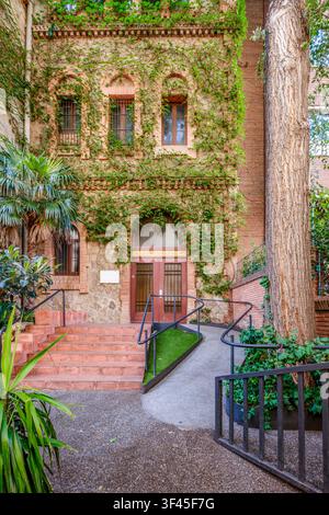 Barcelona – Spanien – 14. Juli 2026: Gebäudeeingang mit Steintreppen, Behindertenzufahrt, Kletter-Efeu, Steinfassade, roten Türen, städtische Architektur Stockfoto